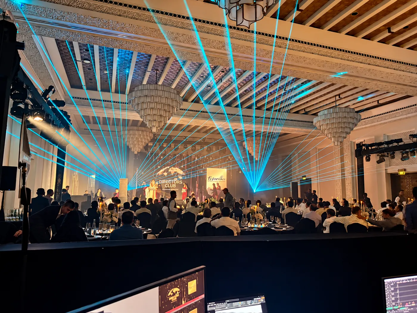 Blue laser beams across a ballroom event with a central stage and LED screen.