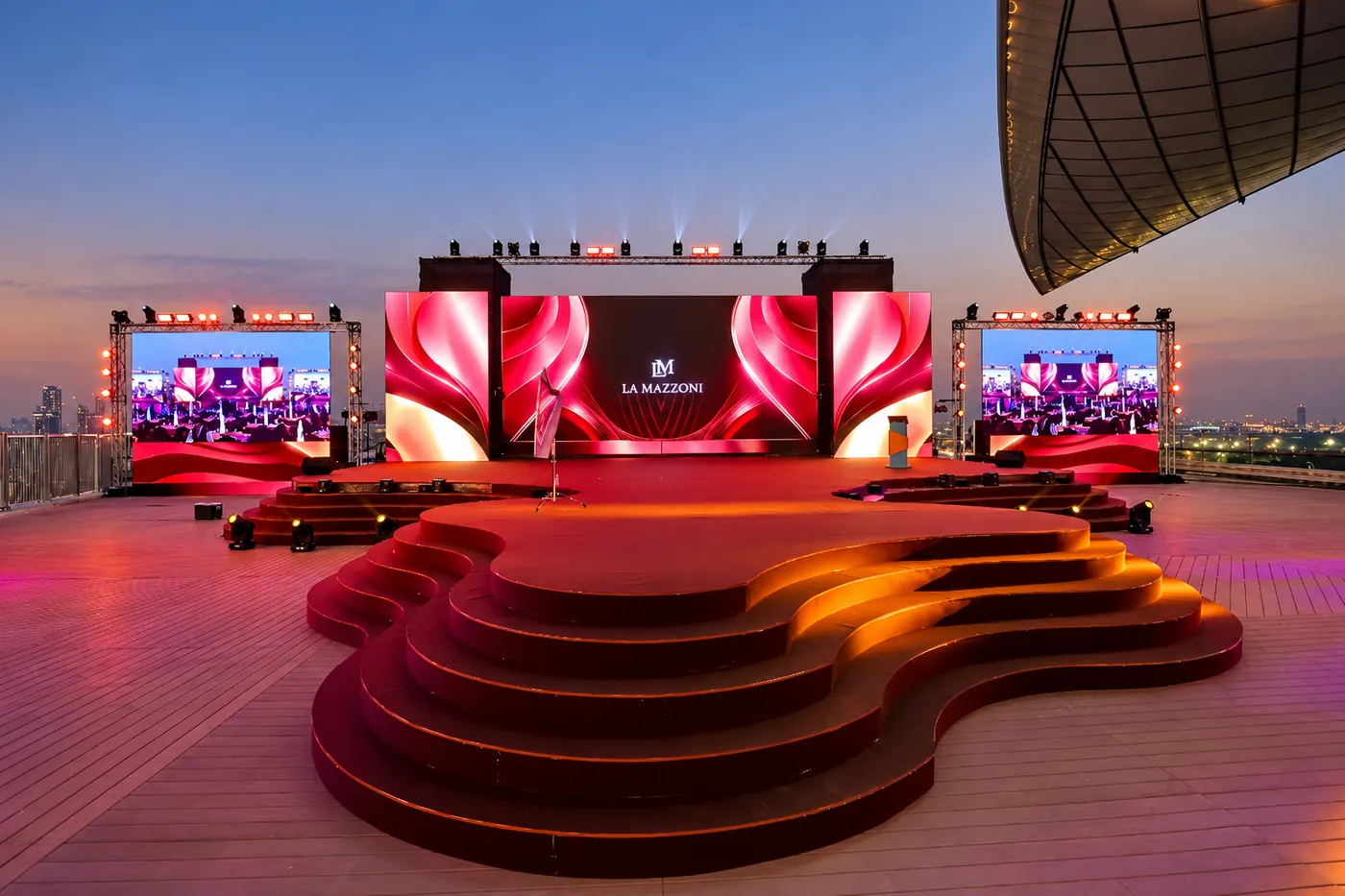 An outdoor presentation stage with a curved platform, LED screens and overhead lighting.
