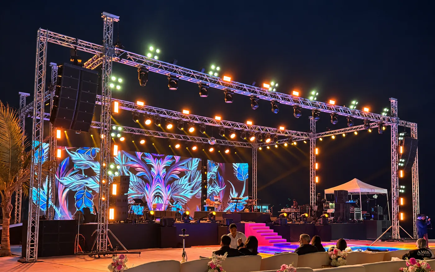 An outdoor stage with LED screens, suspended speakers and a lighting truss.