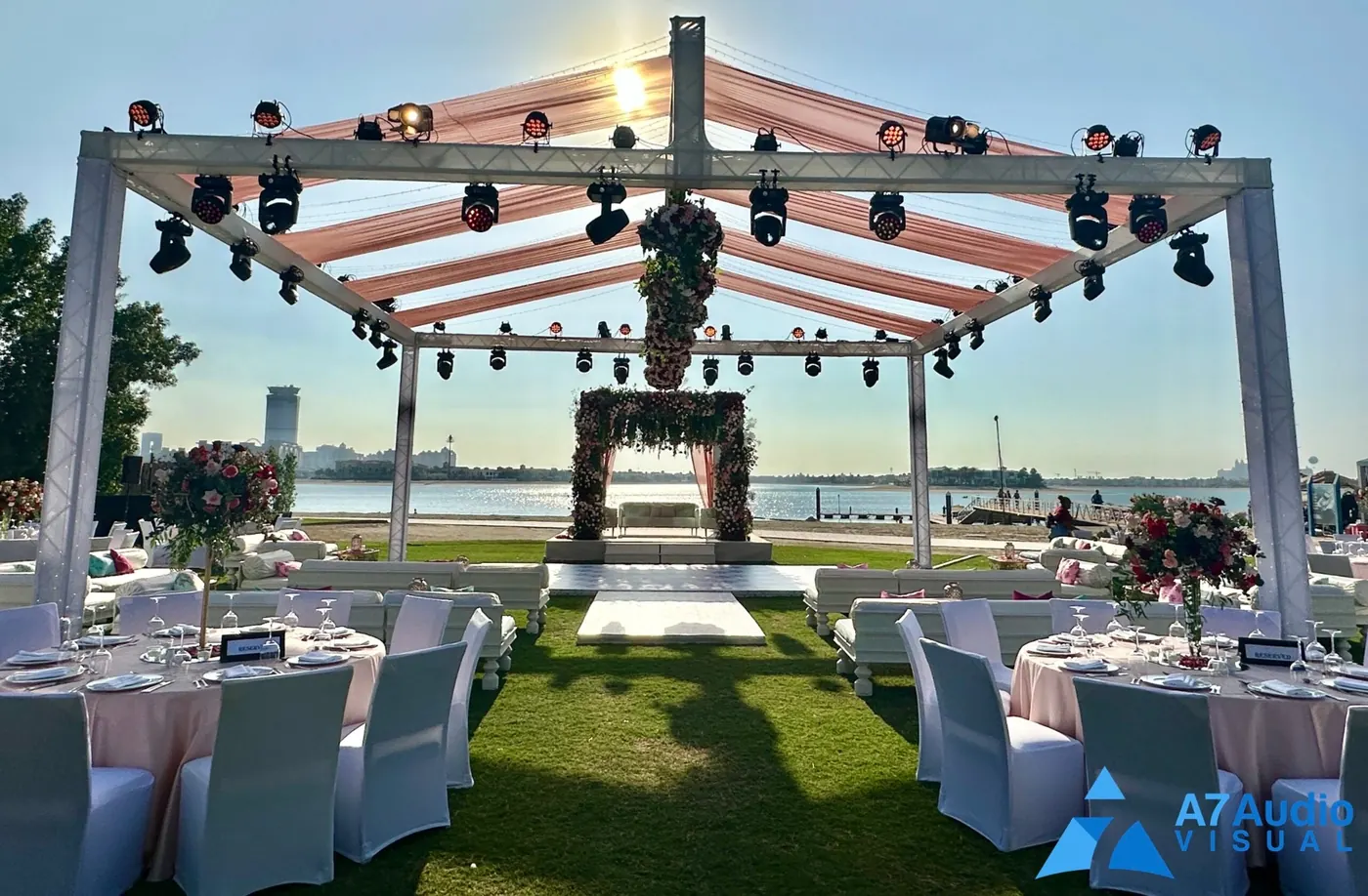 A waterfront wedding setup with covered box truss, lighting fixtures and floral decoration.